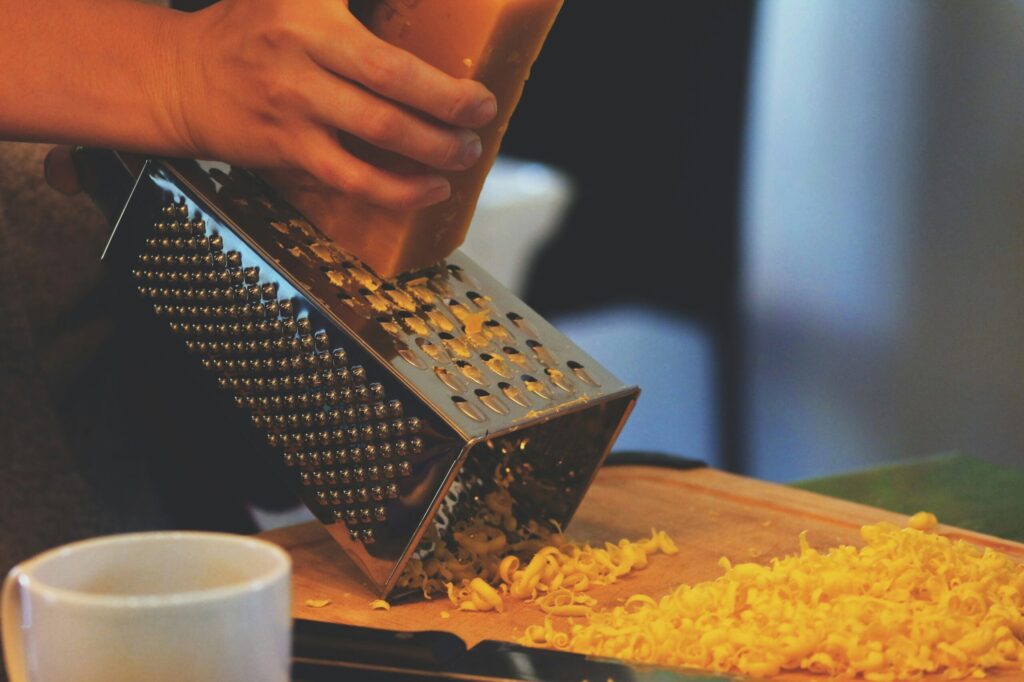 Someone grating a block or red cheese with a cheese grater onto a board