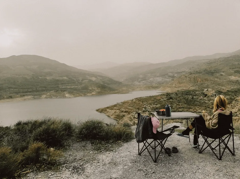 Person sat on camping chair at table looking at a river and hills