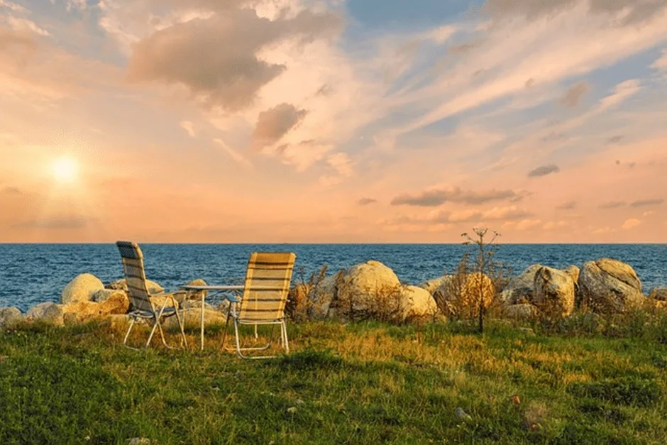 Two deck chairs on grass facing water and rocks