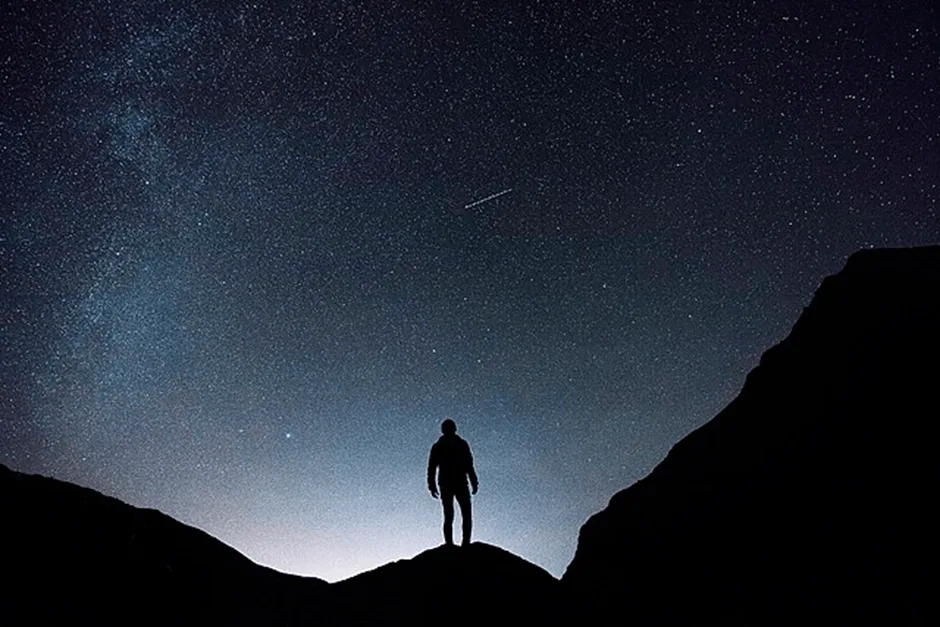 Person stood looking at shooting star in the night sky