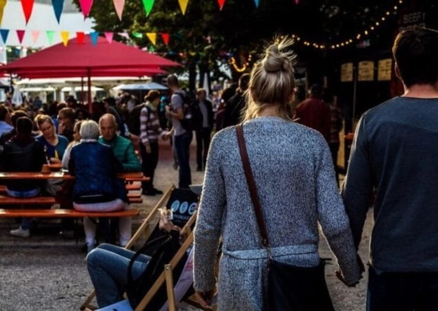 Couple holding hands walking through a campervan festival filled with people