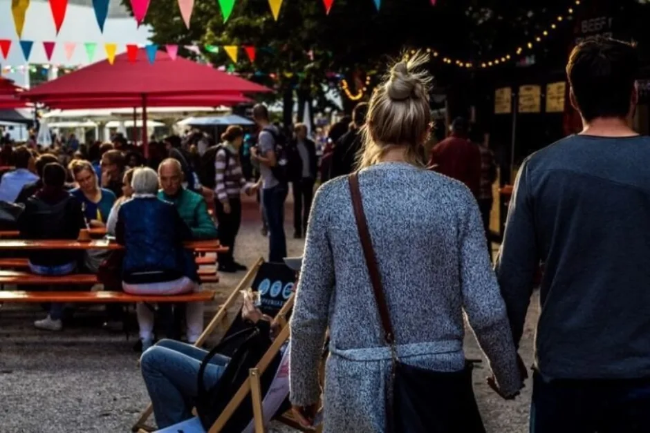 Couple holding hands walking through a campervan festival filled with people