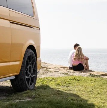 Couple sat on a cliff next to a yellow camper van