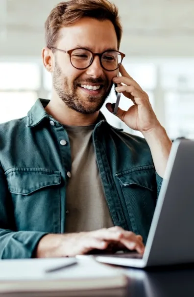 A man on a laptop holding a phone