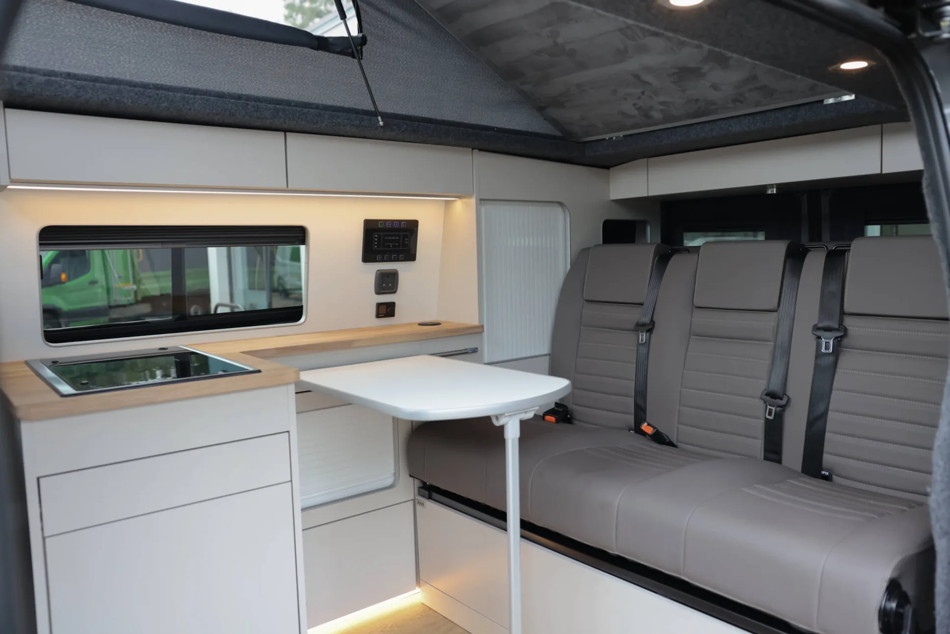 Interior of a campervan with three seats, small white table and sink