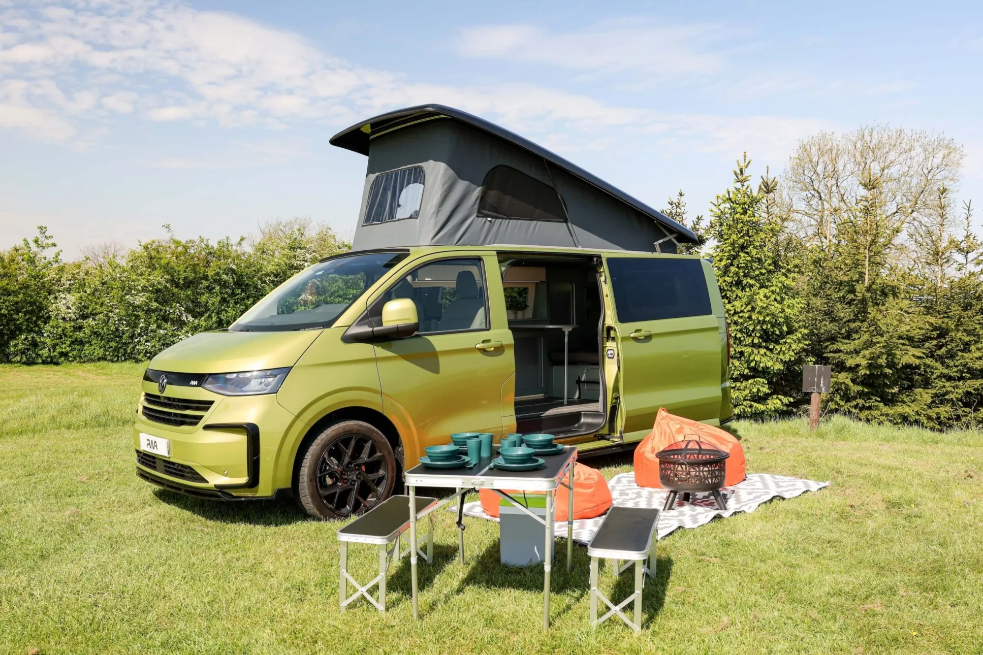 A green campervan with pop top roof and picnic table outside