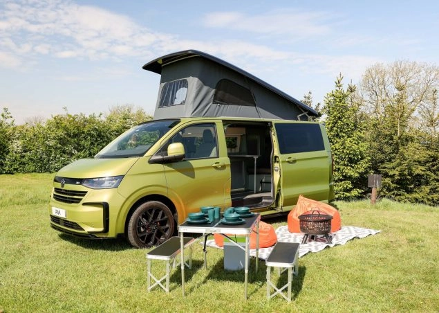A green campervan with pop top roof and picnic table outside